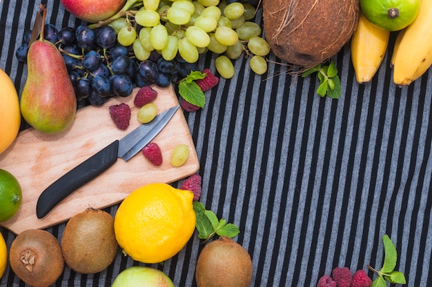 Knife on chopping board with various type of fresh fruits on striped pattern tablecloth