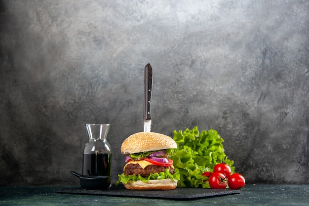 Knife in delicious meat sandwich and green pepper on black tray sauce on gray surface