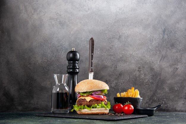 Knife in delicious meat sandwich and green pepper on black tray sauce ketchup tomatoes with stem fries on gray surface