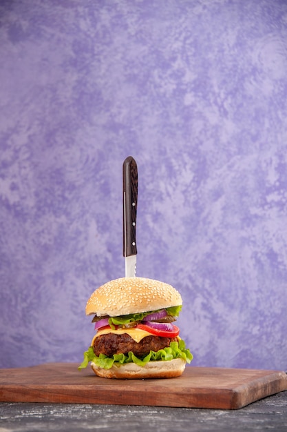 Knife in delicious meat sandwich on wooden cutting board on isolated ice surface with free space