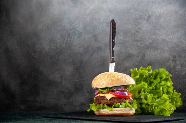 Knife in delicious sandwich and green on black tray on the left side on half dark light surface with free space