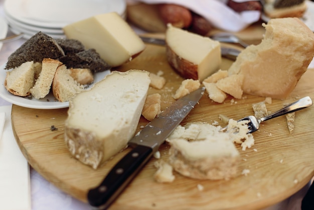 Нож и вилка лежат на деревянной тарелке с различными видами сыров
