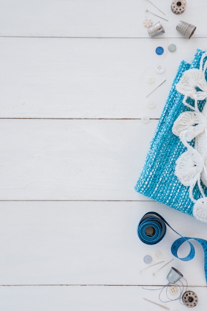 Free photo knitted fabric; thimble; button; needle; measuring tape and push pins on wooden desk