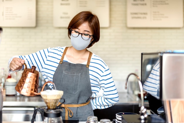 カフェでドリップコーヒーを注ぐフェイスマスクの韓国のバリスタ