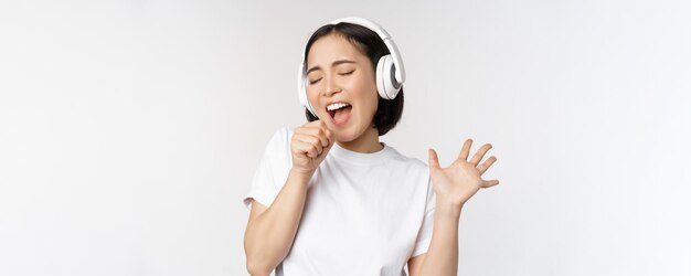 Korean girl sings and listents music in headphones having fun stands over white background