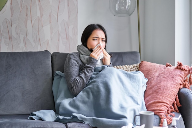 Korean woman feels unwell sneezing and coughing catching cold staying at home with fever and tempera
