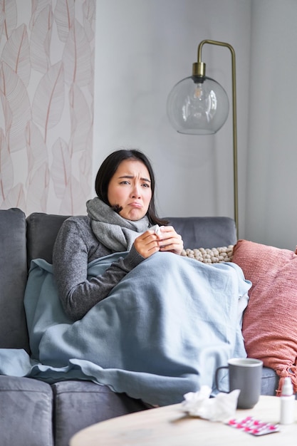 Free photo korean woman feels unwell sneezing and coughing catching cold staying at home with fever and temperature taking medication