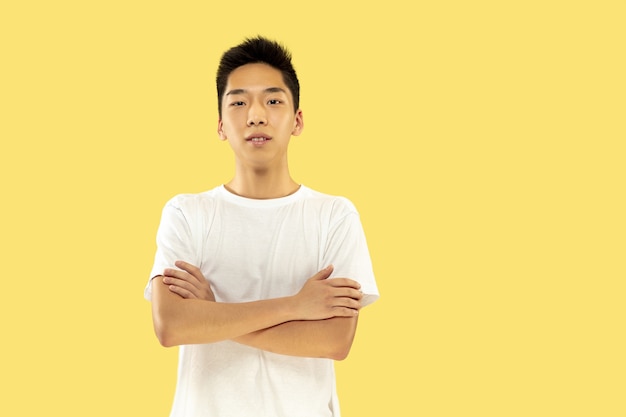 Поясной портрет корейского молодого человека на желтом студийном фоне. Мужская модель в белой рубашке. Стою и смотрю. Понятие о человеческих эмоциях, выражении лица. Передний план. Модные цвета.
