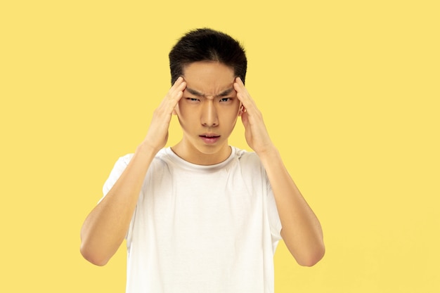 Korean young man's half-length portrait on yellow studio background. Male model in white shirt. Thinking serious. Concept of human emotions, facial expression. Front view. Trendy colors.