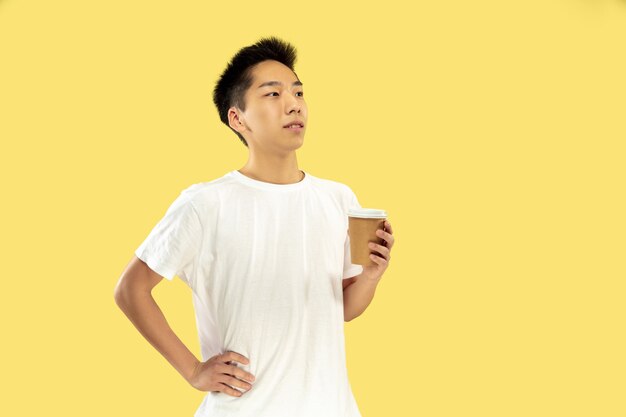 韓国の若者の肖像画。白いシャツの男性モデル。コーヒーを飲み、幸せを感じます。人間の感情、顔の表情の概念。正面図。トレンディな色。