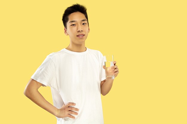 韓国の若者の肖像画。白いシャツの男性モデル。水を飲んでいる。人間の感情、顔の表情の概念。正面図。トレンディな色。