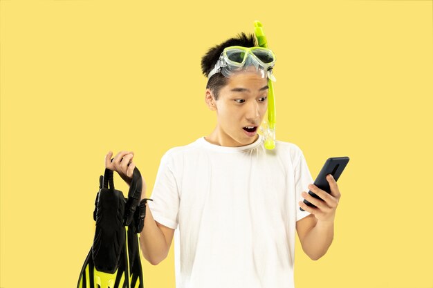 Korean young man's portrait. Male model in white shirt and goggles. Holding flippers. Concept of human emotions, expression, summertime, vacation, weekend.