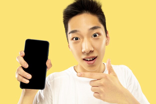 한국 청년의 초상화. 흰 셔츠에 남성 모델. 베팅, 뉴스 읽기 또는 대화를 위해 스마트 폰을 사용합니다. 인간의 감정, 표정의 개념.