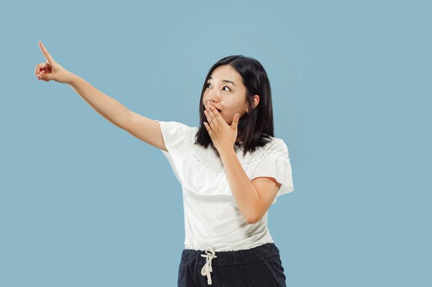 Korean young woman's half-length portrait on blue  space. Female model in white shirt. Showing and pointing something.