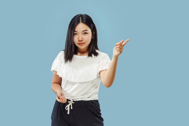 韓国の若い女性の半身像。白いシャツの女性モデル。何かを見せて指し示す。人間の感情、顔の表情の概念。正面図。