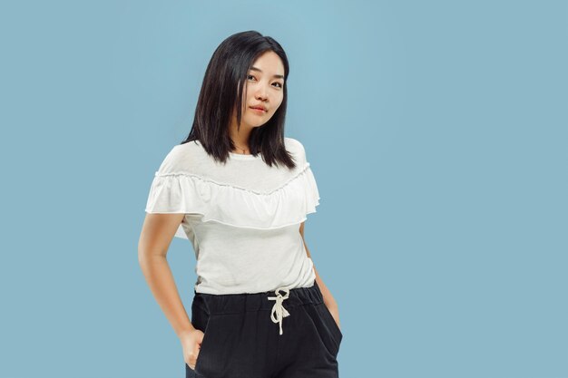 Korean young woman's half-length portrait. Female model in white shirt. Standing and smiling. Concept of human emotions, facial expression. Front view.