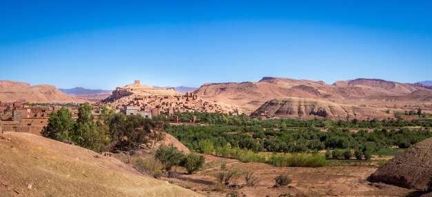 Ксар Айт-Бен-Хадду в окружении зелени под солнечным светом и голубым небом в Марокко