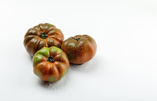 Kumato tomatoes on white wall, high angle view.