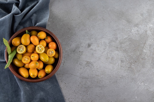 Kumquat fruits in a bowl on a pieces of fabric, on the marble table.