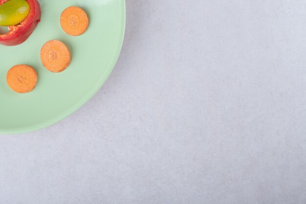 Kumquat, slice pepper and sliced carrot on plate on marble table.