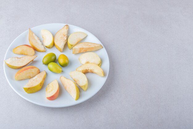 Kumquat and sliced apple on a plate on marble table.