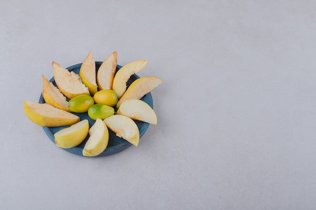 Кумкват и нарезанное яблоко на деревянной тарелке на мраморном столе.