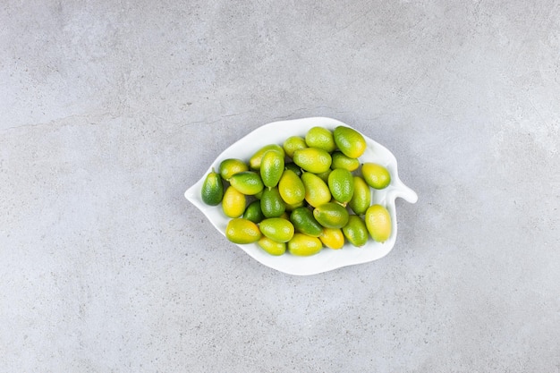 Kumquats piled on a ornate plate on marble surface