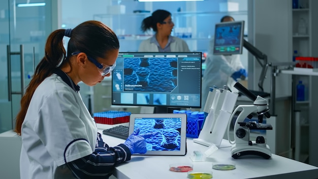 Lab technician doctor analyzing virus evolution looking on digital tablet. Team of scientists conducting vaccine development using high tech for researching treatment against covid19 pandemic.