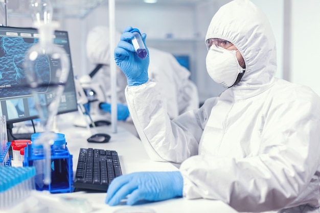 Lab technician dressed in protective suit as safety precaution looking at test tube