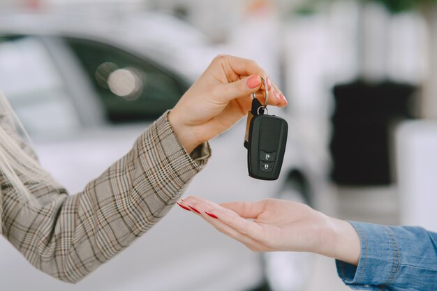 Ladies in a car salon. Woman buying the car. Elegant woman in a blue dress. Manager give keys to the client.