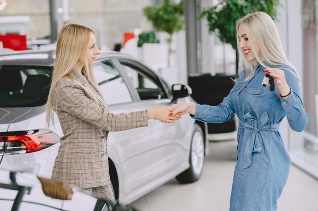 カーサロンの女性。車を買う女性。青いドレスを着たエレガントな女性。マネージャーはクライアントにキーを渡します。