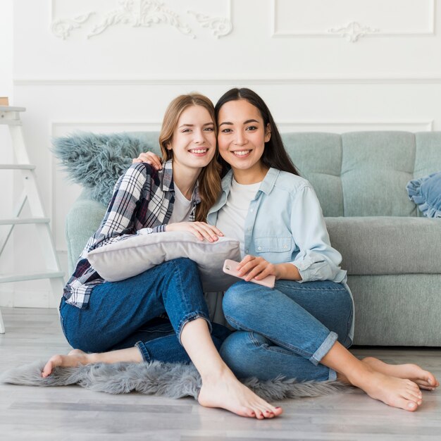 Ladies sitting embracing on floor barefoot with pillow and mobile phone