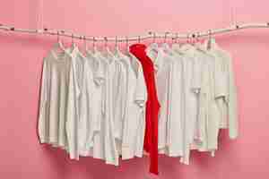 無料写真 ハンガーにアレンジされたレディースの白いカジュアルな服、赤いニットの暖かいセーターはコレクション全体の中で際立っています。ピンクの背景にぶら下がっているドレッシングセット。ホームワードローブ。クラシックなスタイル。ファッションショップ