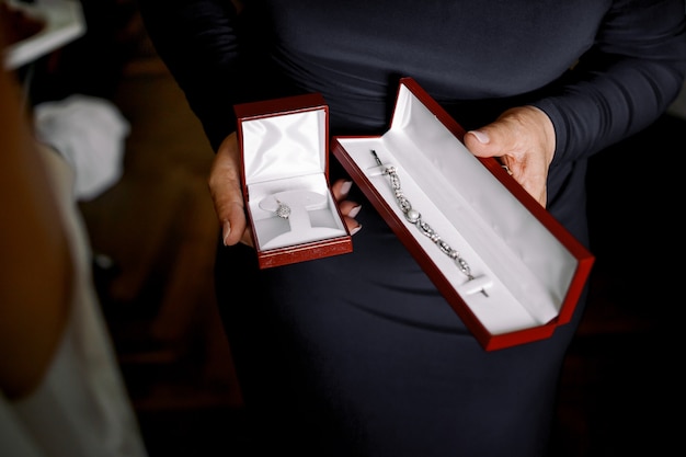 Lady in black dress holds red velvet boxes with jewels