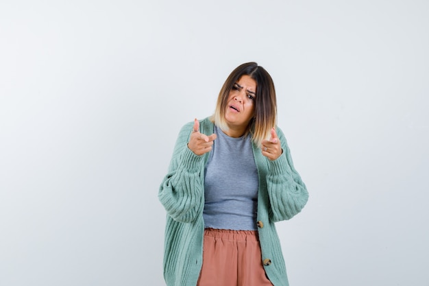 Lady in casual clothes pointing at camera and looking puzzled , front view.