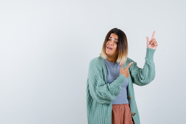 Lady in casual clothes pointing up and looking hesitant , front view.