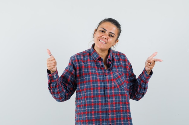 Lady in casual shirt pointing away, showing thumb up and looking happy , front view.