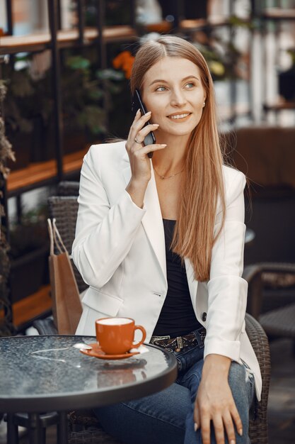 女性はコーヒーを飲みます。テーブルに座っている女性。女の子は電話を使います。