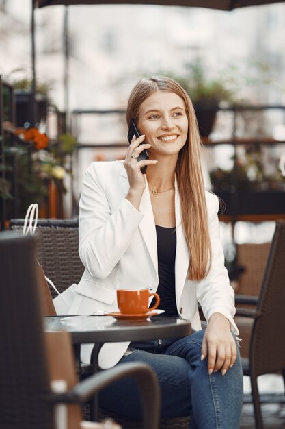 Lady drinks a coffee. Woman sitting at the table. Girl use a phone.