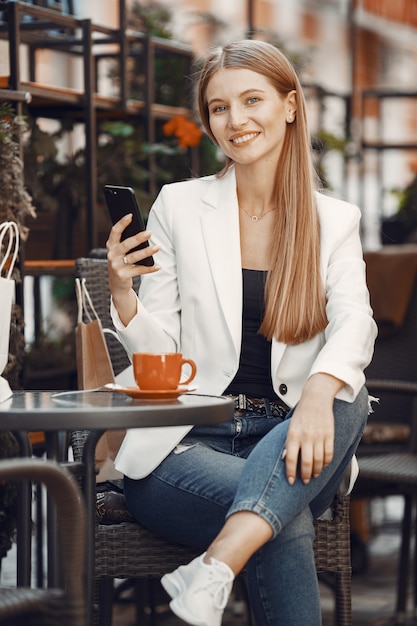 Lady drinks a coffee. Woman sitting at the table. Girl use a phone.