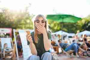 Foto gratuita signora che mangia il gelato che ride. ritratto di giovane donna seduta in un parco in una giornata di sole a mangiare il gelato