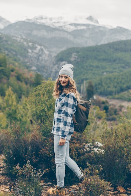 lady in gray hat and jeans standing and smiling in nature during daytime