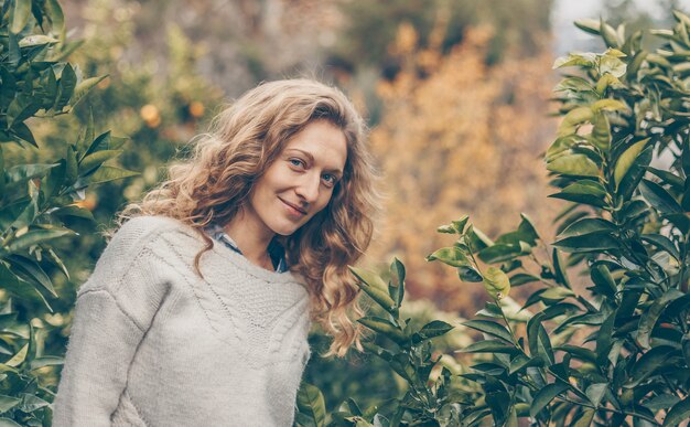 lady in gray sweater standing and smiling in nature during daytime
