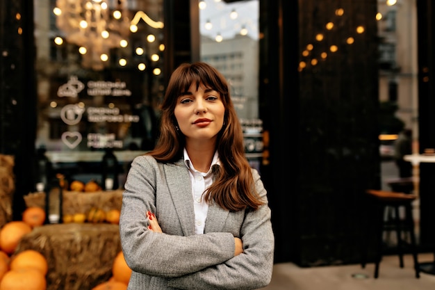 Lady in grey suit smiling at camera on background of stylish cafe with lights.