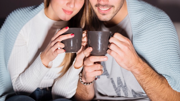 Free photo lady and guy in coverlet with mugs in dark room