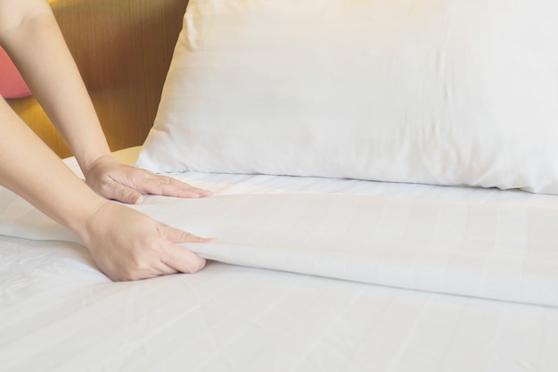 Lady hands set up white bed sheet in hotel room