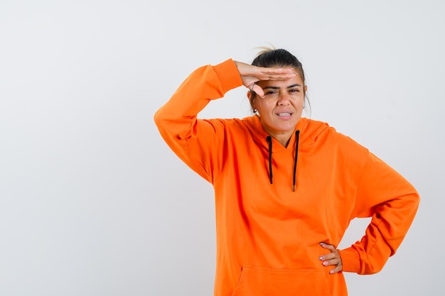 Lady holding hand over head in orange hoodie and looking focused