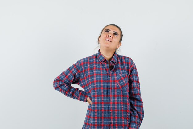 Lady holding hand on waist in casual shirt and looking hesitant , front view.