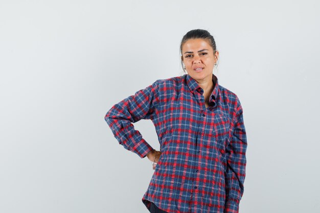 Lady holding hand on waist in casual shirt and looking pensive. front view.