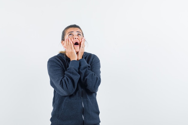 Lady holding hands on cheeks in hoodie and looking confused 